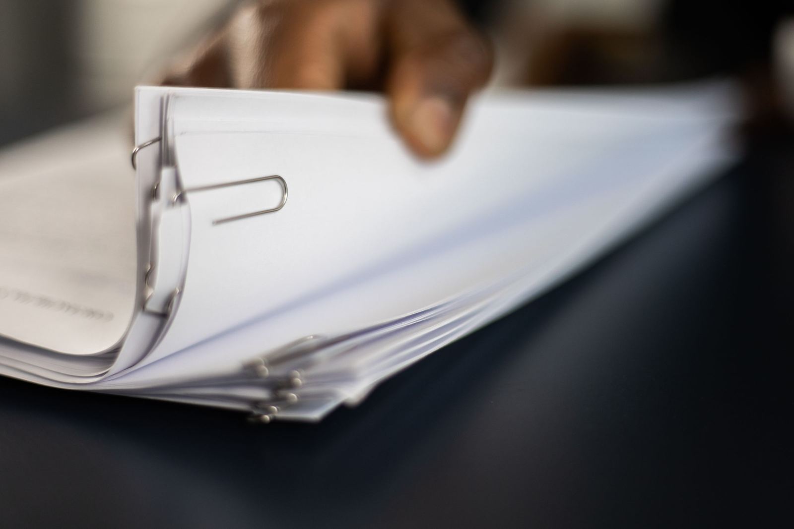 A hand leafing through a thick stack of documents
